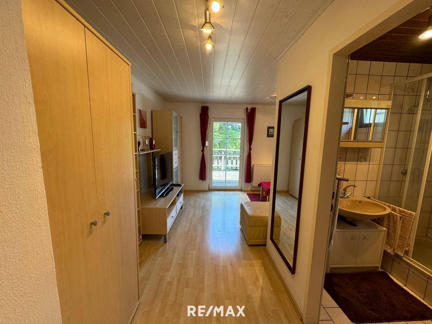 Flur mit Holzschrank, Spiegel und Blick in den Wohnbereich sowie ein angrenzendes Badezimmer.