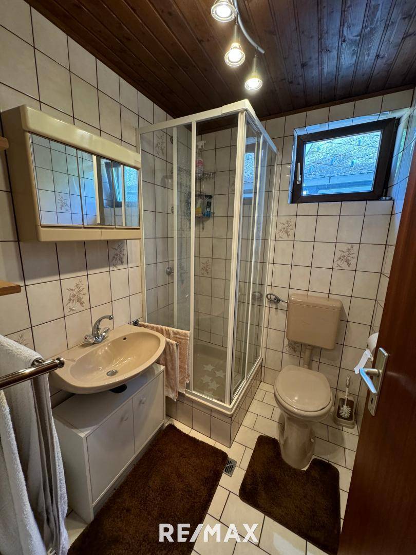Gefliestes Badezimmer mit Duschkabine, Waschbecken, WC und Fenster, in einem funktionalen Design.