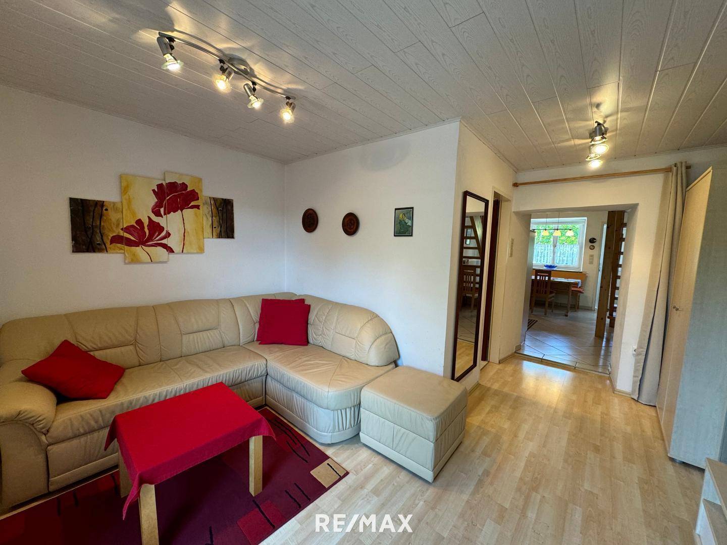 Gemütliches Wohnzimmer mit beigefarbenem Ecksofa, Holzboden und Deckenpaneelen, ideal zum Entspannen.