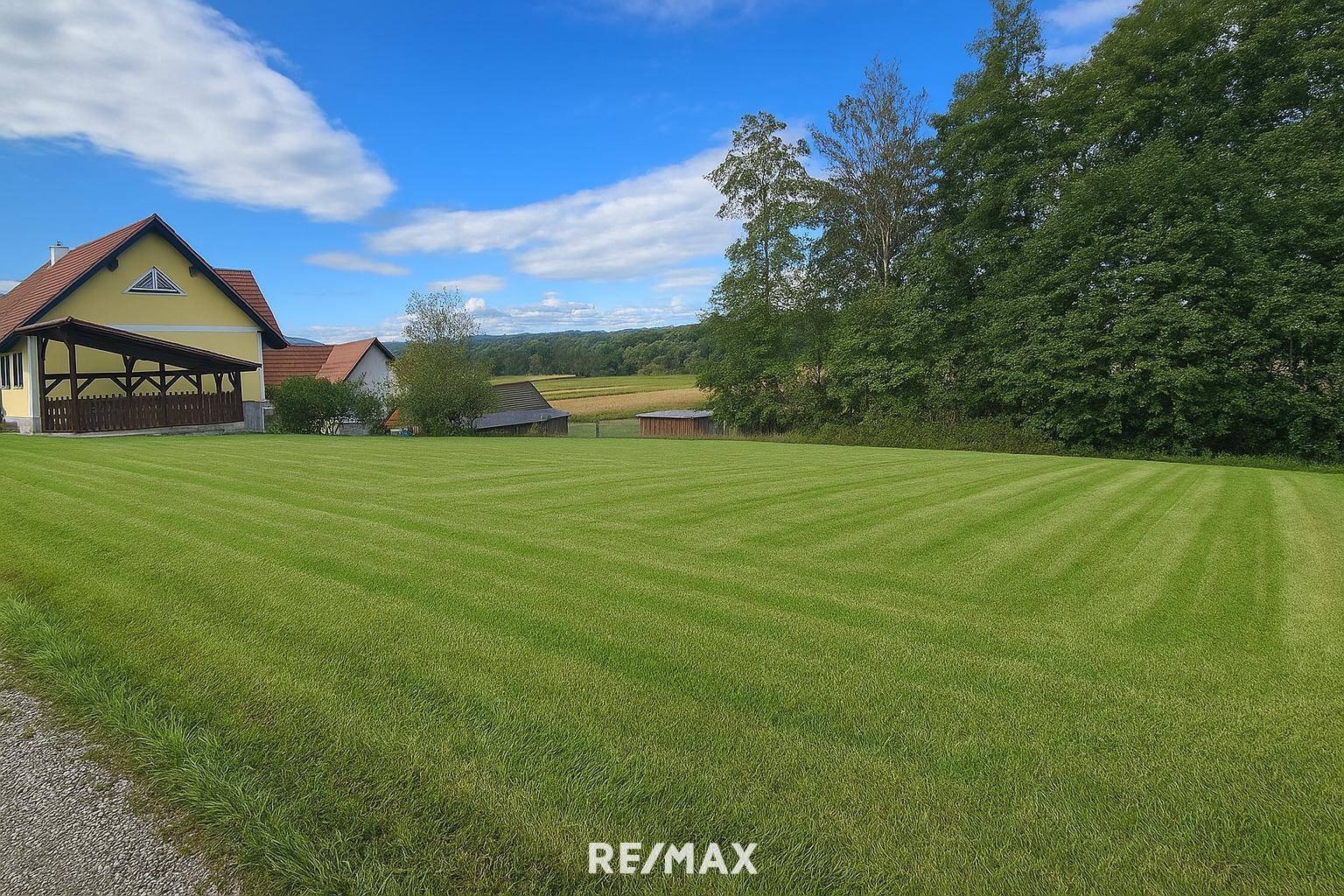 Weitläufige, frisch gemähte Rasenfläche mit einem charmanten Haus und ländlicher Umgebung unter blauem Himmel.