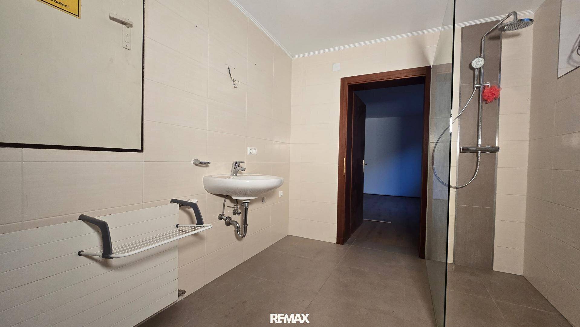 Funktionales Badezimmer mit beigefarbenen Fliesen, Dusche und barrierefreien Elementen.
