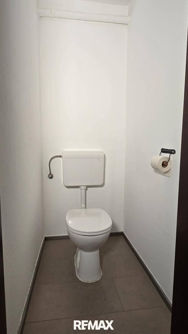 Kleines separates WC mit weißer Toilette und grauen Bodenfliesen.