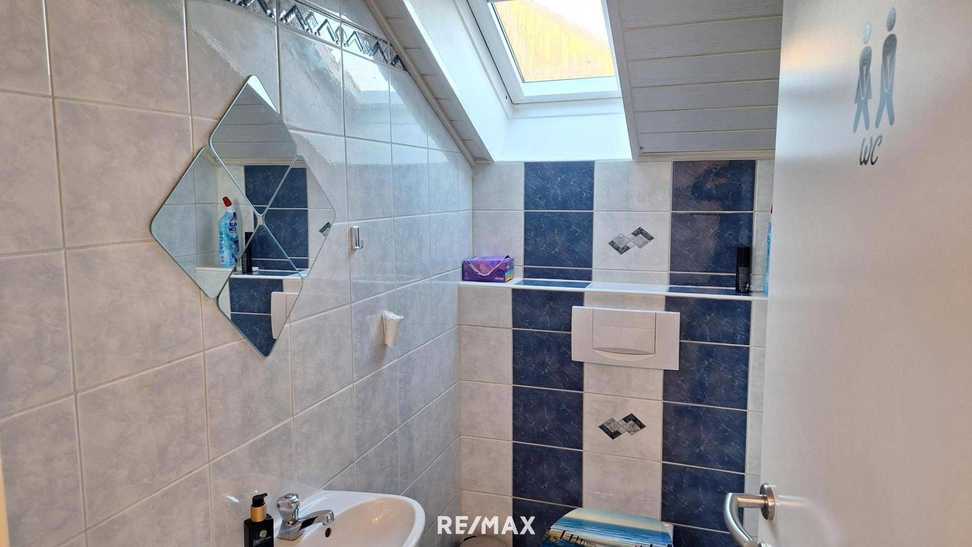 Kleines WC mit Waschbecken, Toilette und dekorativen blau-weißen Fliesen im Dachgeschoss.