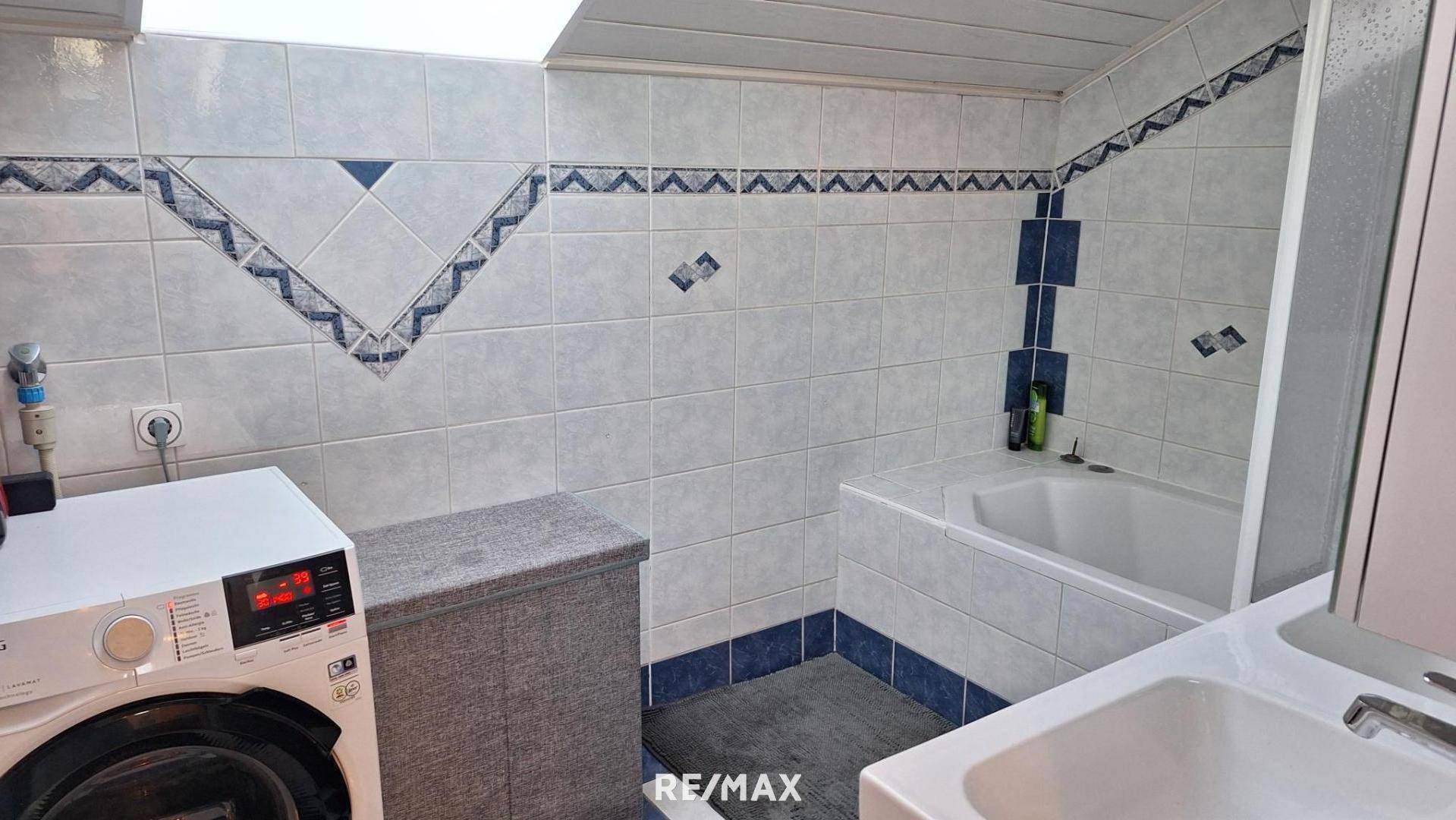 Badezimmer mit Badewanne, Waschbecken und Waschmaschine, gefliest in Weiß und Blau.