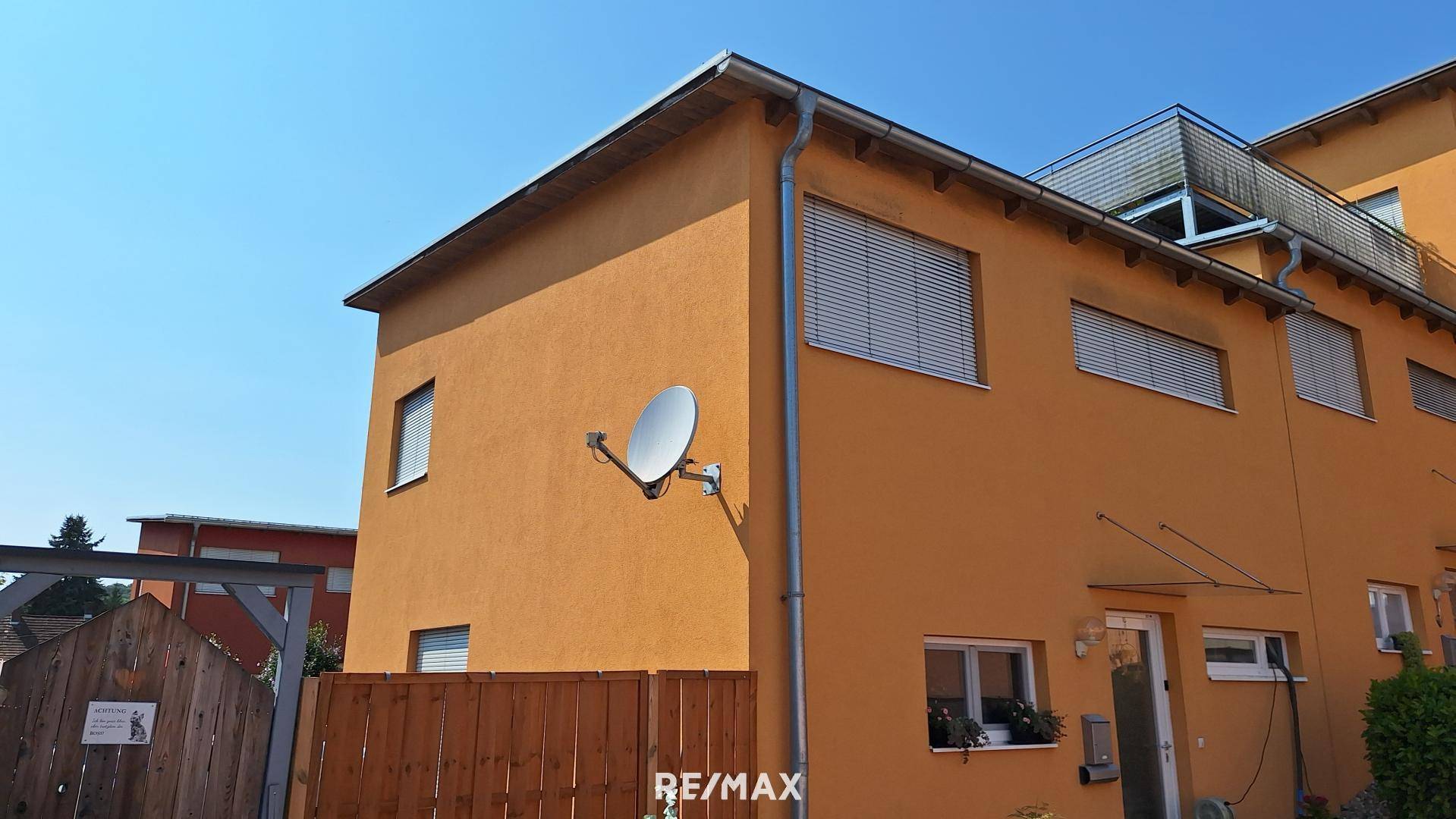 Gelb-orange Hausfassade mit Fenstern, Rollläden und einer Satellitenschüssel an der Wand.