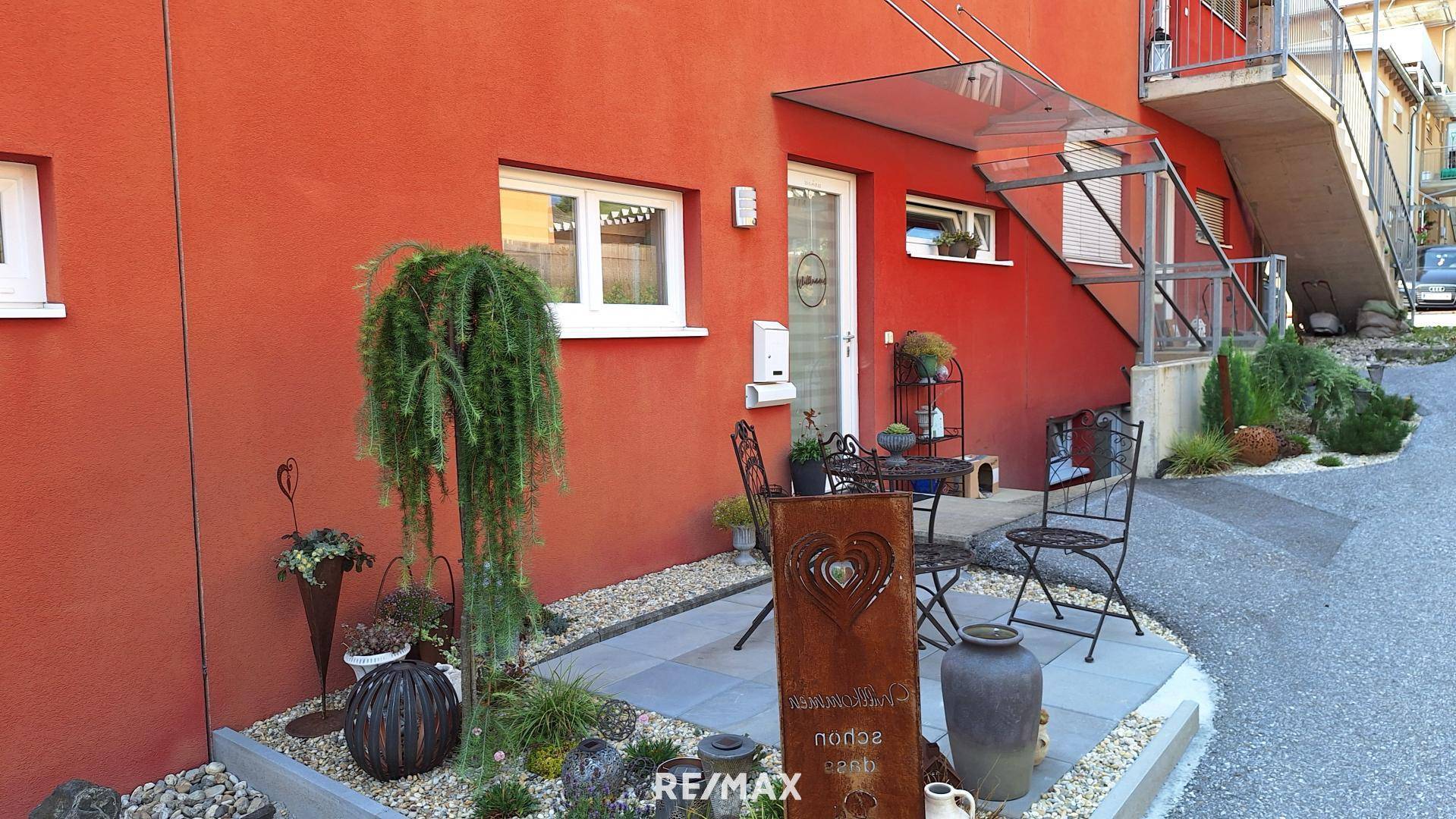 Eingangsbereich des Hauses mit roter Fassade, dekorativen Pflanzen und einem kleinen Sitzplatz.