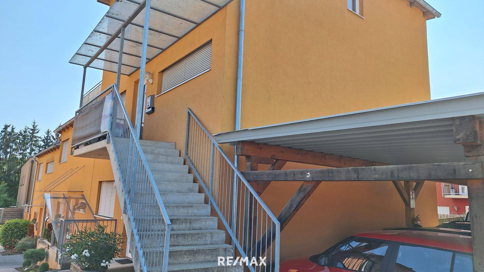 Gelb-orange Hausfassade mit Außentreppe, Carport und Zugang zu den oberen Etagen.