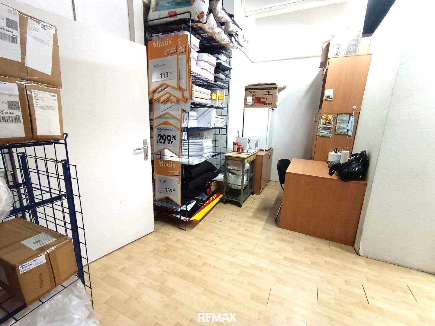Kleiner Bürobereich mit Schreibtisch, Regalen und Lagerkartons, ausgestattet mit Holzfußboden.