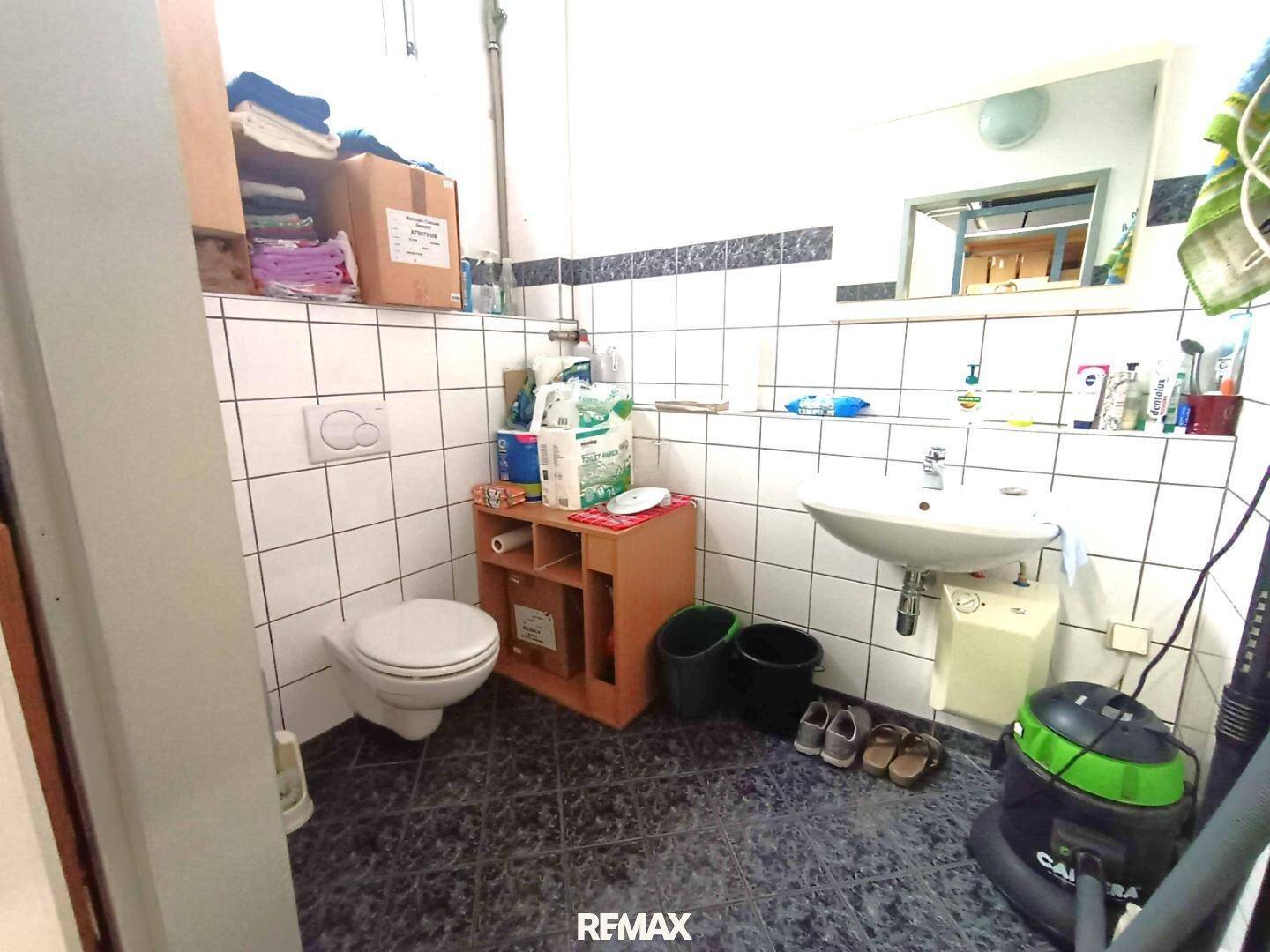 Einfaches Badezimmer mit Toilette, Waschbecken und weiß-schwarz gefliesten Wänden.
