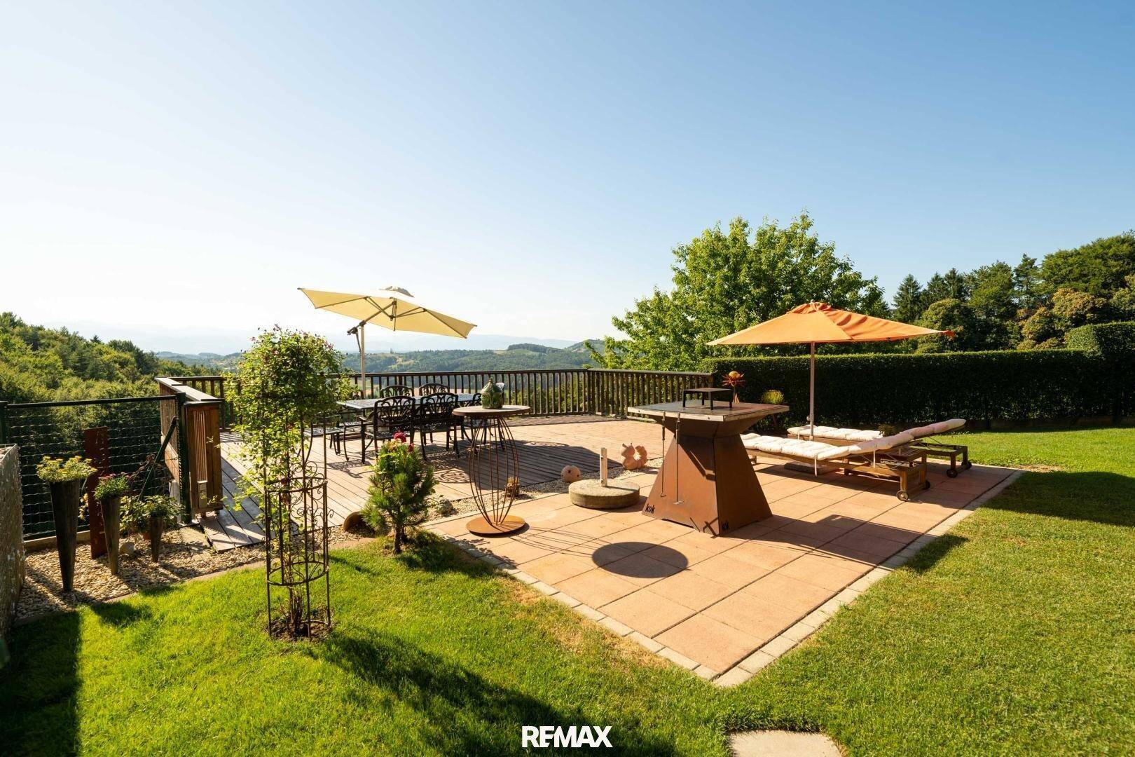 Große Sonnenterrasse mit Gartenmöbeln, Sonnenschirmen und weitem Blick über die Landschaft.