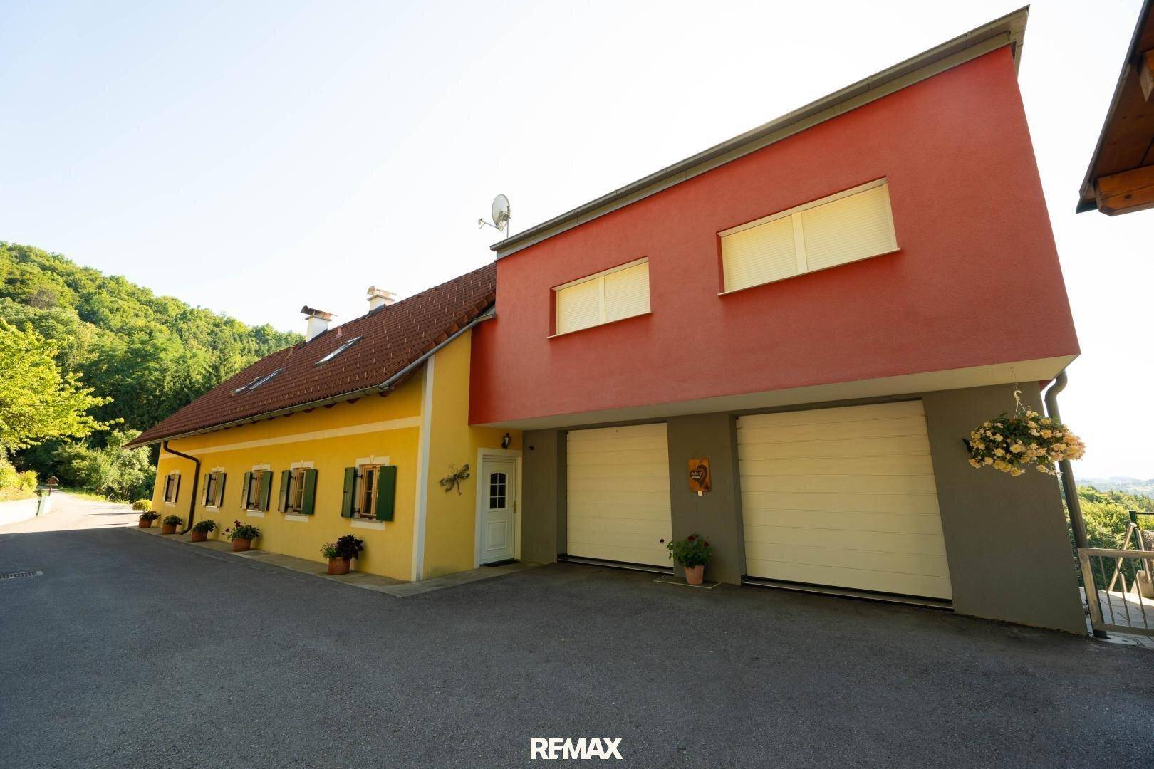 Anwesen mit gelbem Haupthaus und modernem rotem Anbau mit Garagentoren.