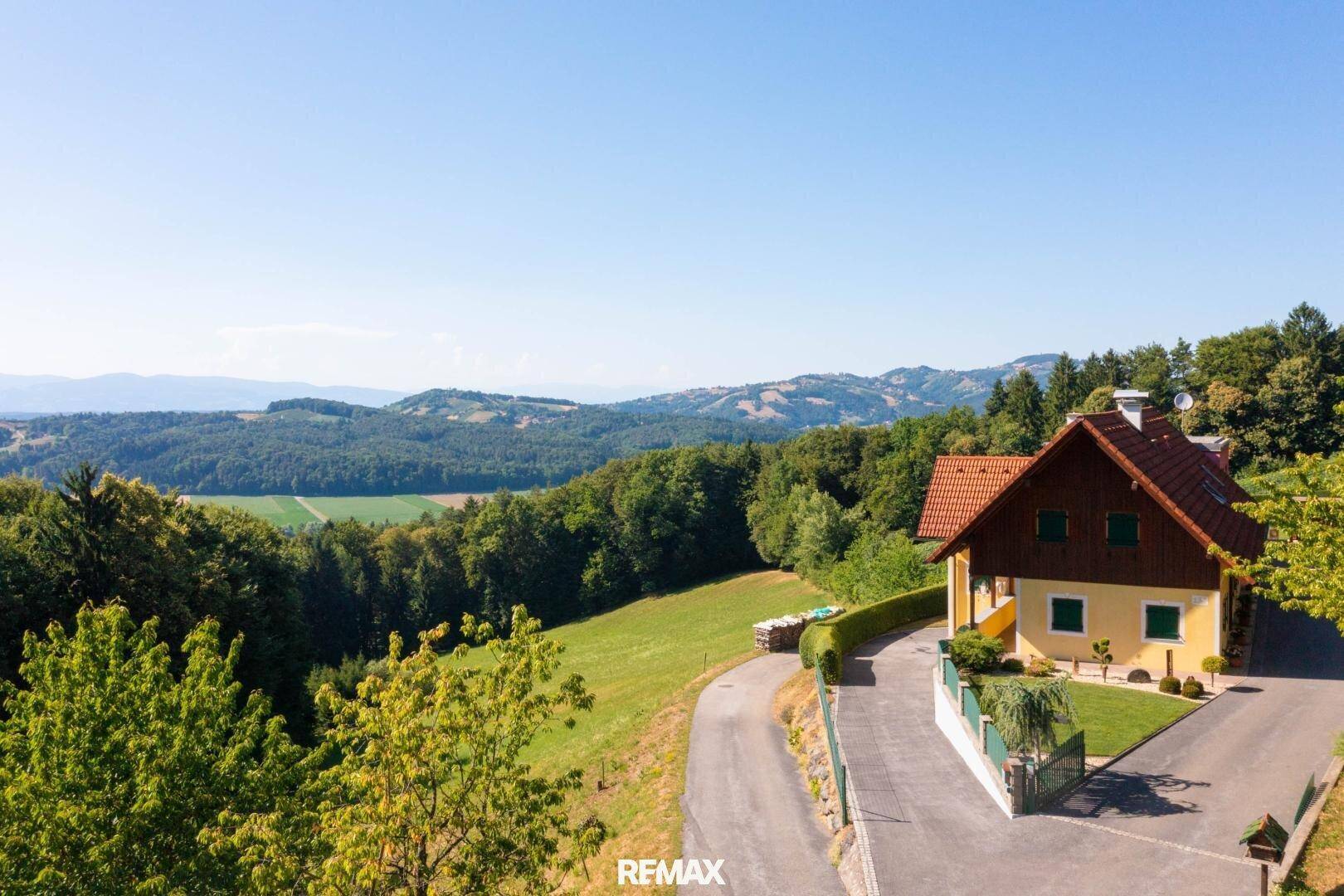 Anwesen mit gepflegtem Garten und Zufahrt, umgeben von grünen Hügeln und Wäldern.