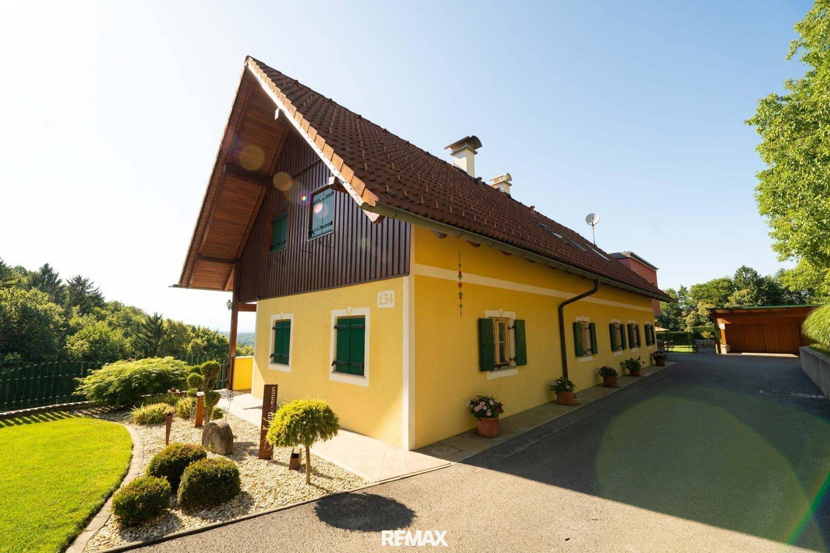 Seitenansicht des gelben Hauses mit grünen Fensterläden und gepflegtem Vorgarten.