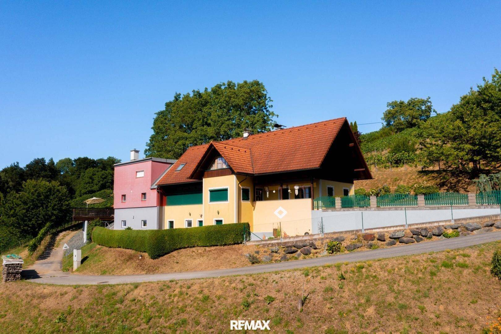 Anwesen mit gelbem Haupthaus und rotem Anbau, umgeben von grüner Natur und Weinbergen.