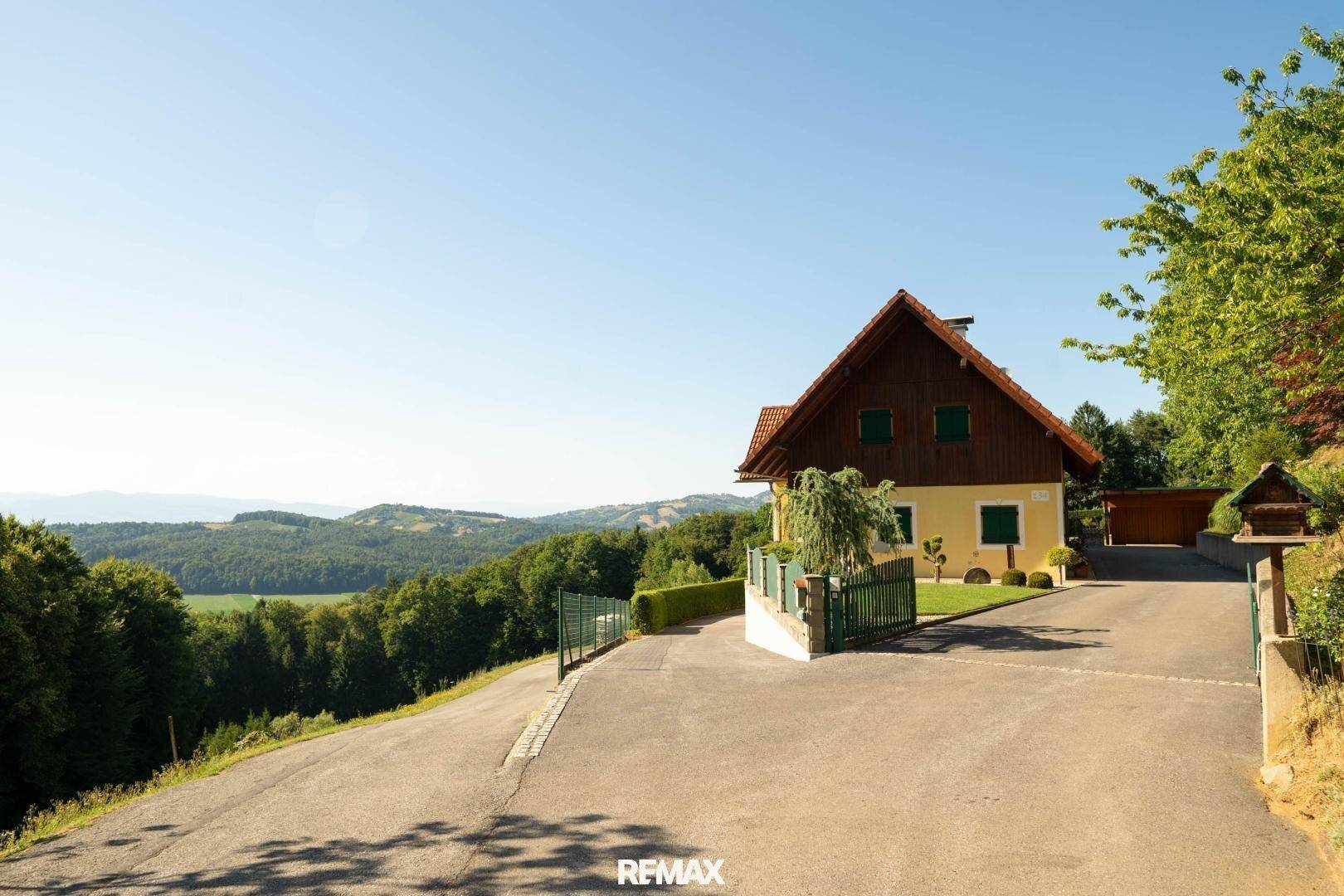 Gelbes Haus mit rotem Dach und gepflegtem Vorgarten an einer Zufahrtsstraße.