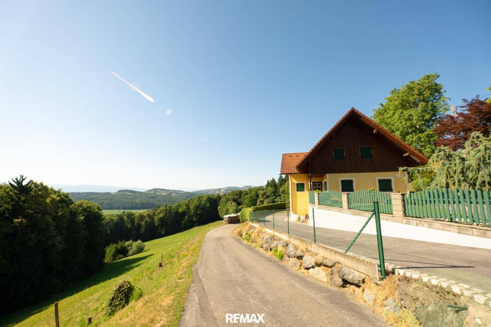 Gelbes Haus mit grünen Fensterläden an einer Zufahrtsstraße mit weitem Landschaftsblick.
