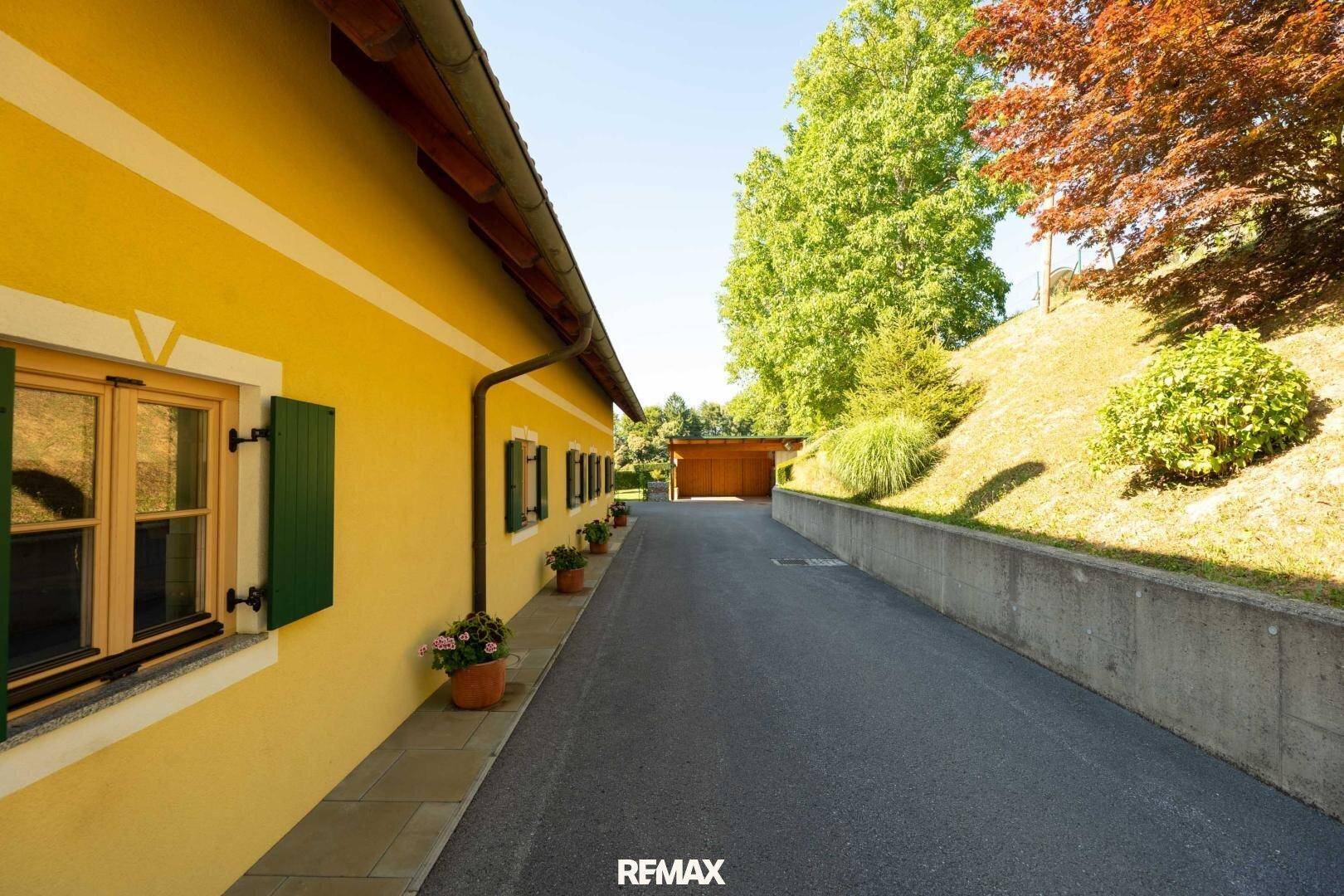 Seitenansicht des gelben Hauses mit Blumenkübeln entlang der Zufahrt und viel Grün.