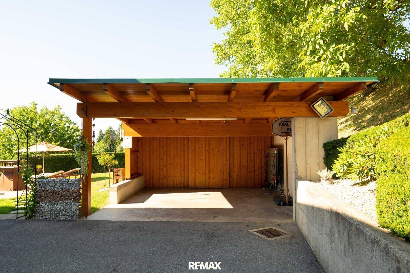 Geräumiger Holzcarport mit Betonboden und angrenzendem Gartenbereich.