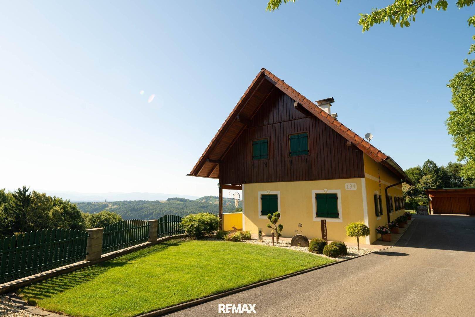 Charmantes gelbes Haus mit grünen Fensterläden und gepflegtem Rasen vor einer weiten Landschaft.