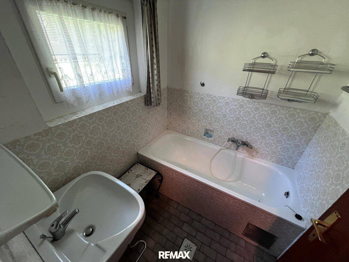 Badezimmer mit Badewanne, Waschbecken, Fenster und gemusterten Fliesen im traditionellen Stil.