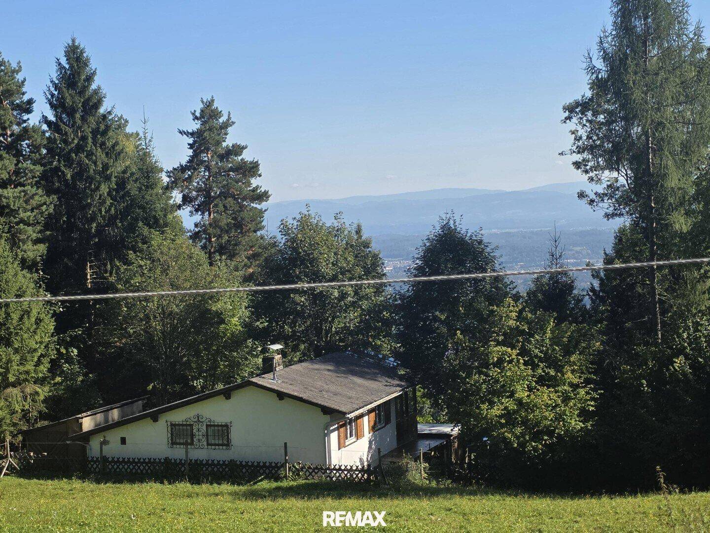 Das Haus eingebettet in grüne Hügel mit weitem Blick auf die umliegende Landschaft und Berge.
