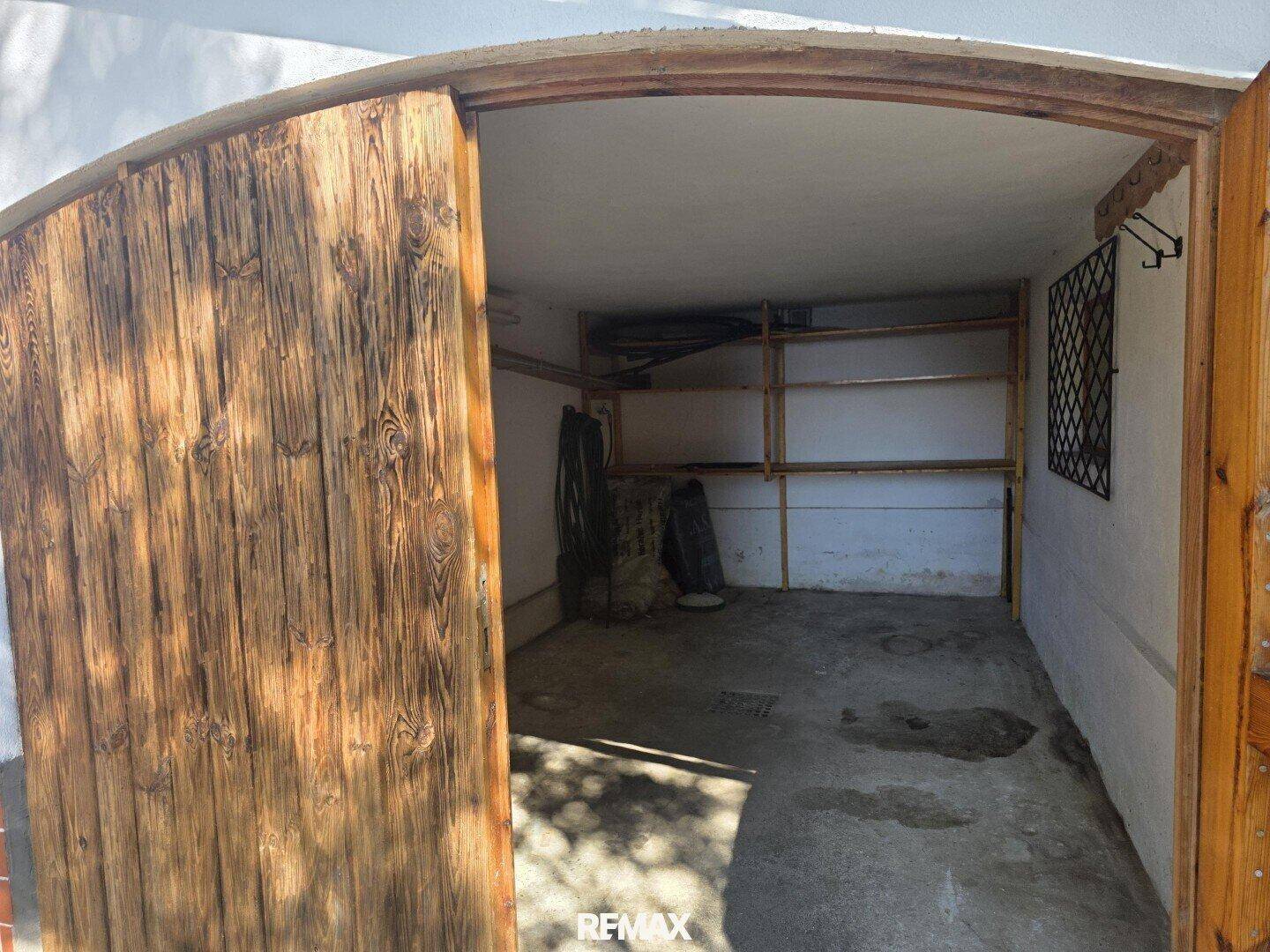 Leere Garage mit Holztoren und Betonboden, bietet Stauraum oder Parkmöglichkeit.