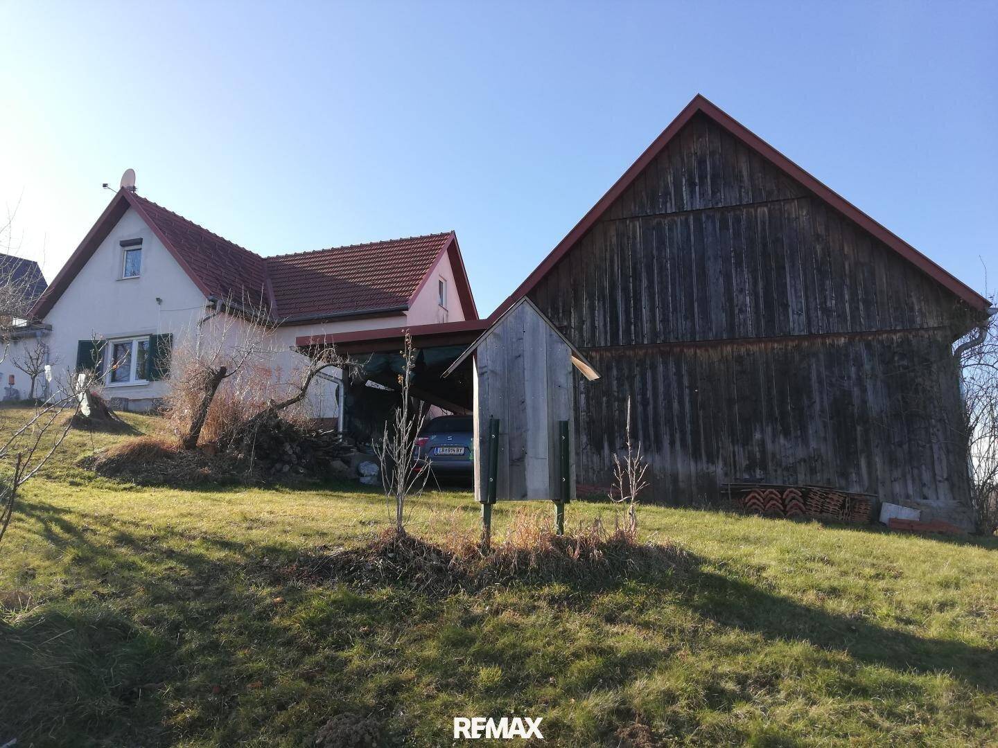 Ländliches Anwesen mit Wohnhaus und angrenzender Scheune auf einem sonnigen Hügel.