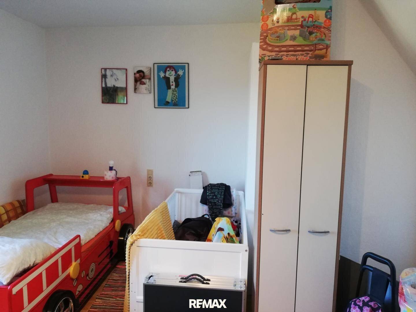 Kinderzimmer mit einem roten Feuerwehrbett, einem Babybett und einem Kleiderschrank.