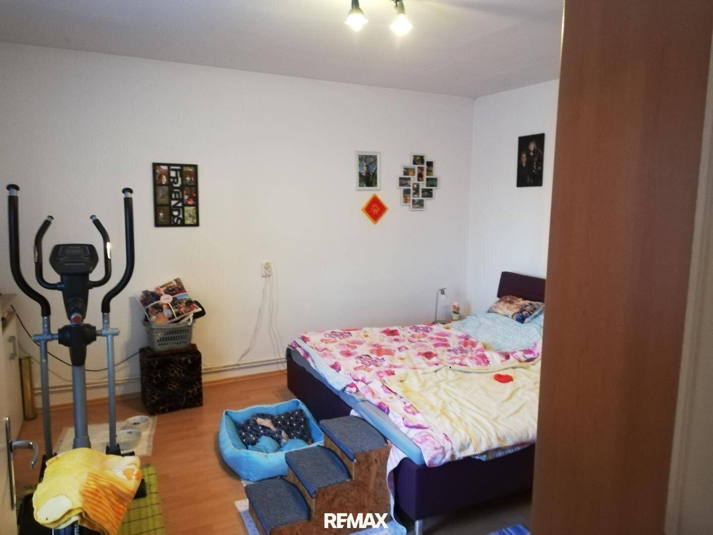 Schlafzimmer mit Doppelbett, Heimtrainer und persönlichen Dekorationen an den Wänden.