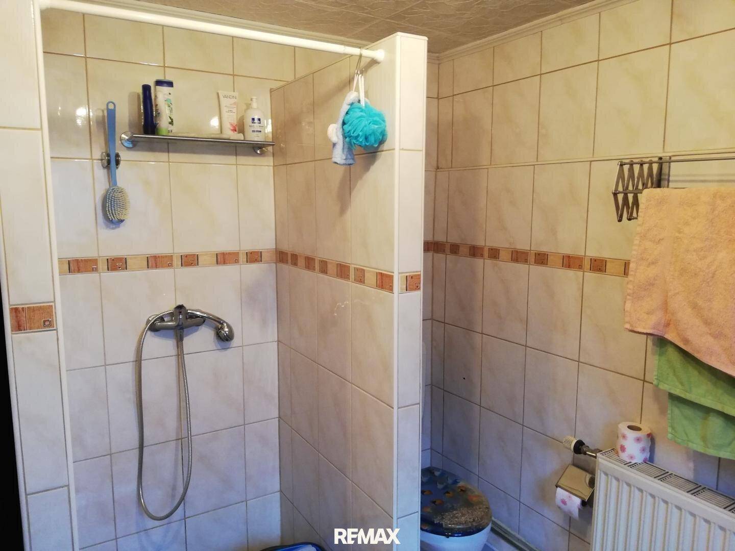 Gefliestes Badezimmer mit Duschbereich und Heizkörper, in einem traditionellen Stil gehalten.