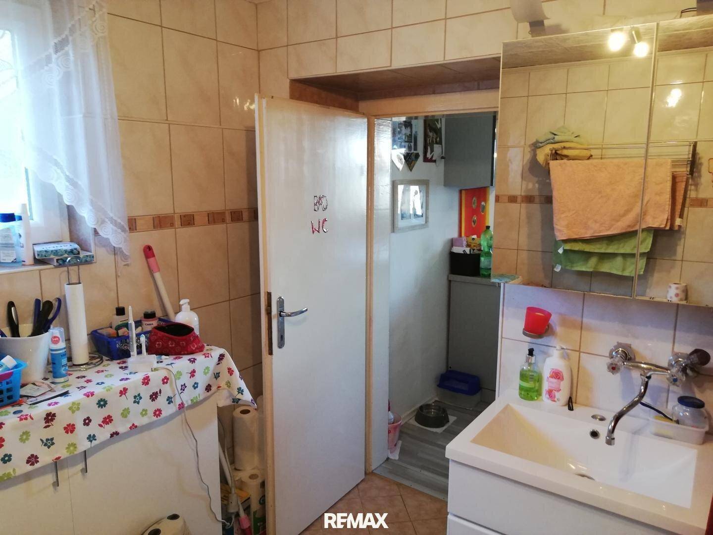Badezimmer mit Waschbecken, Fliesen und Zugang zu einer separaten Toilette.
