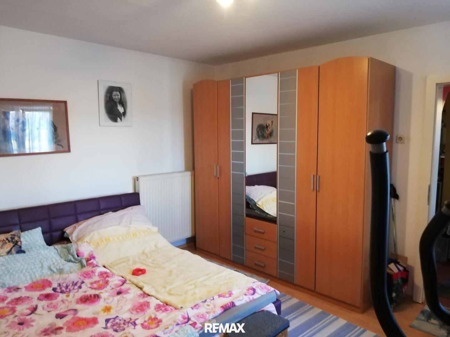 Schlafzimmer mit Doppelbett, großem Kleiderschrank mit Spiegeln und Heimtrainer.