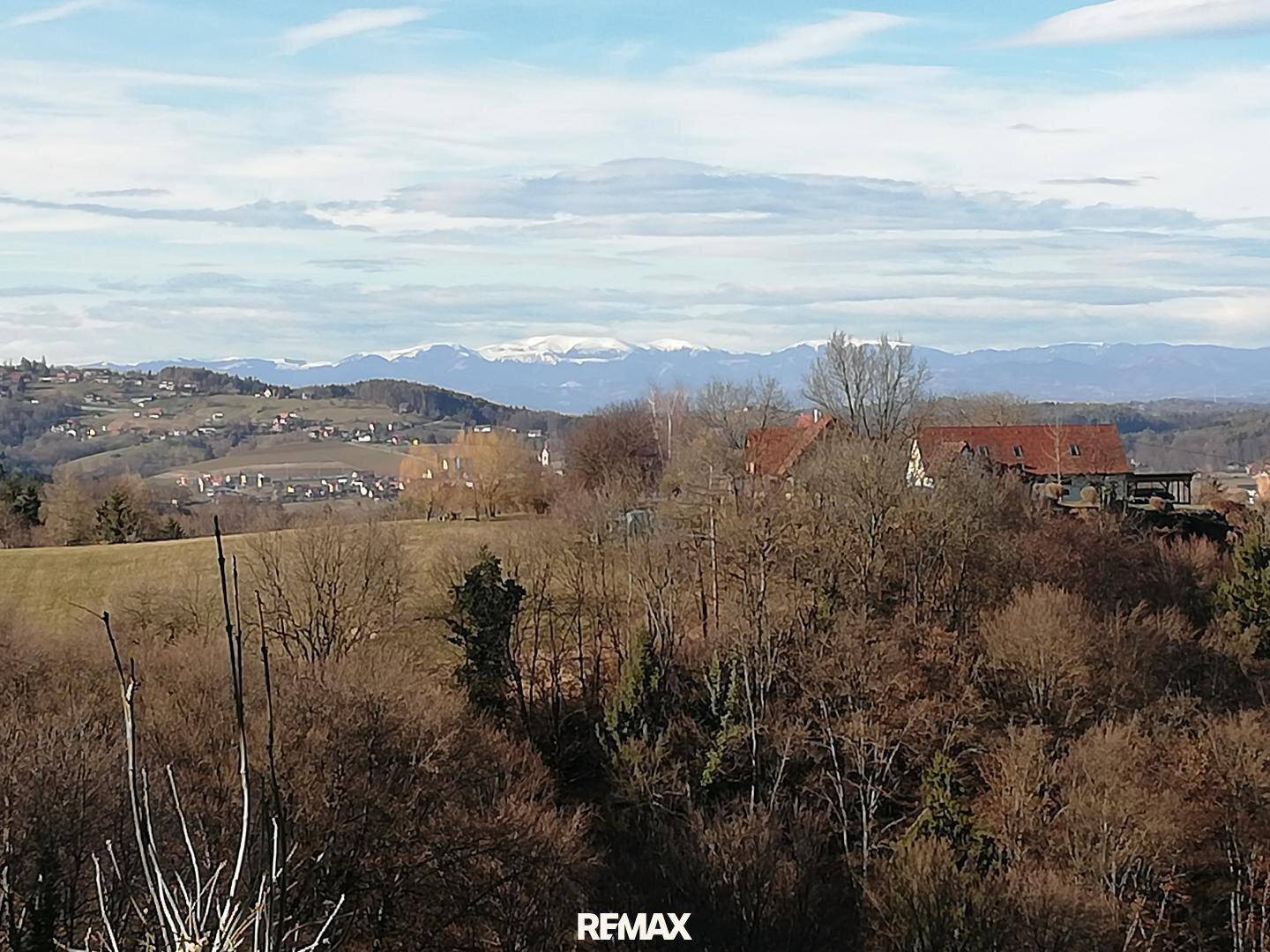 Panoramablick über die hügelige Landschaft mit fernen schneebedeckten Bergen am Horizont.