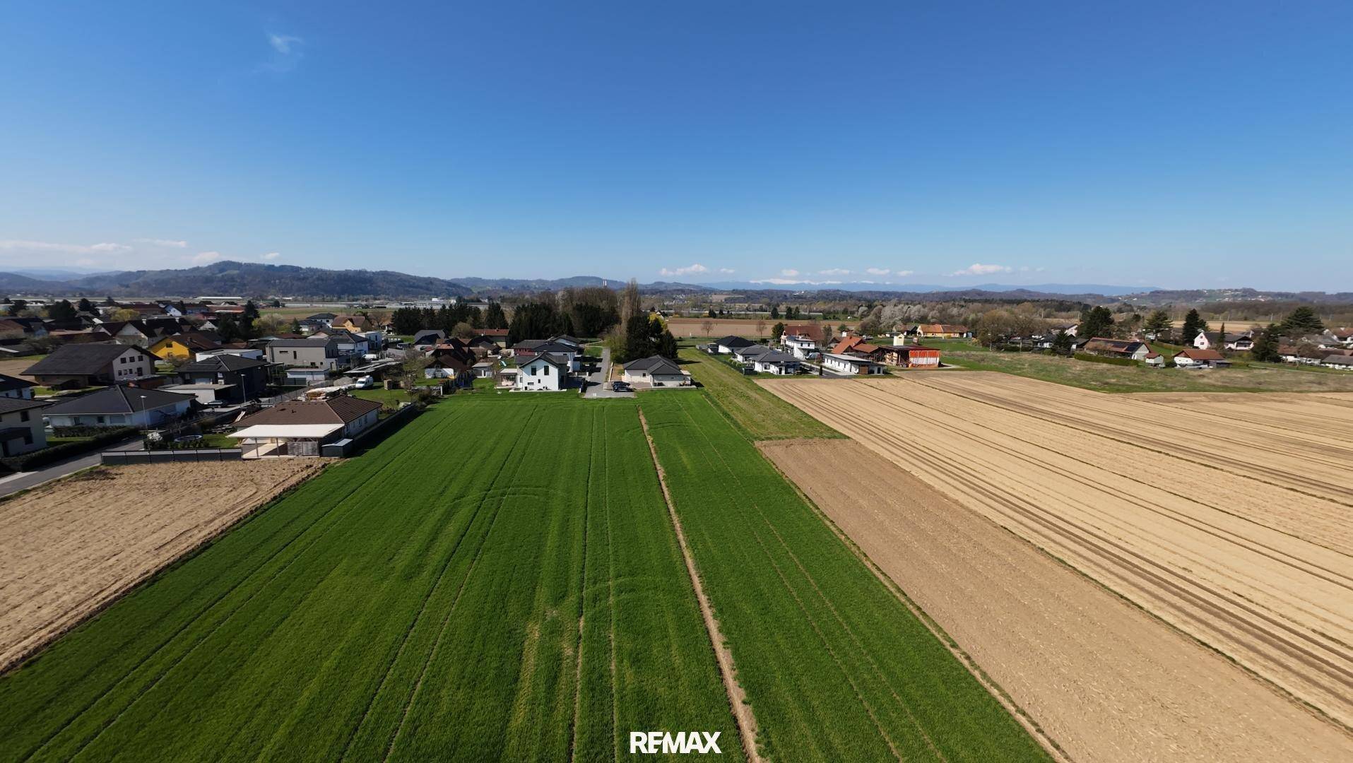 Weitläufige Luftaufnahme einer ländlichen Gegend mit Feldern, Häusern und Bergen im Hintergrund.