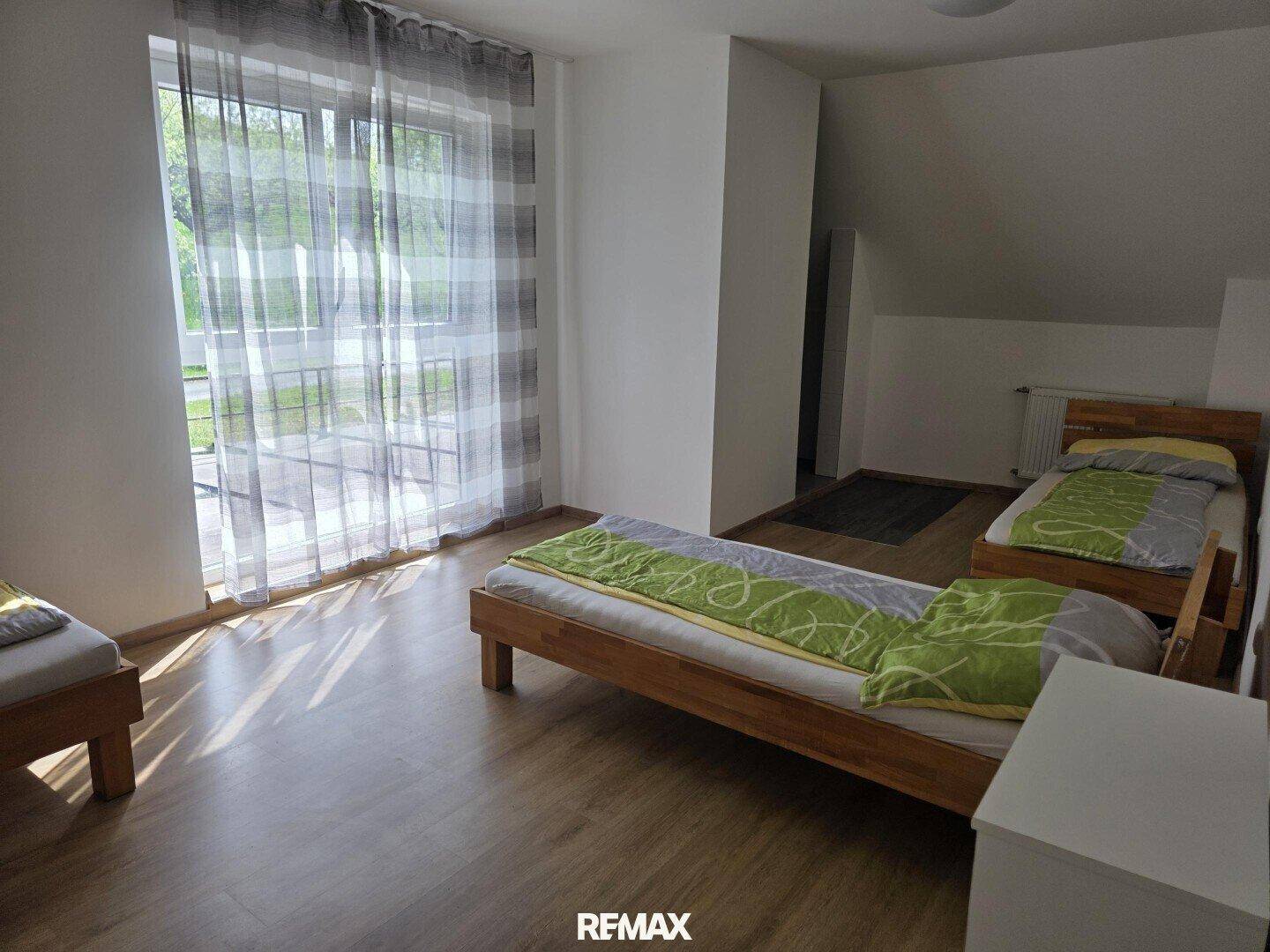 Helles Schlafzimmer mit drei Einzelbetten, Laminatboden und Zugang zu einem Balkon.