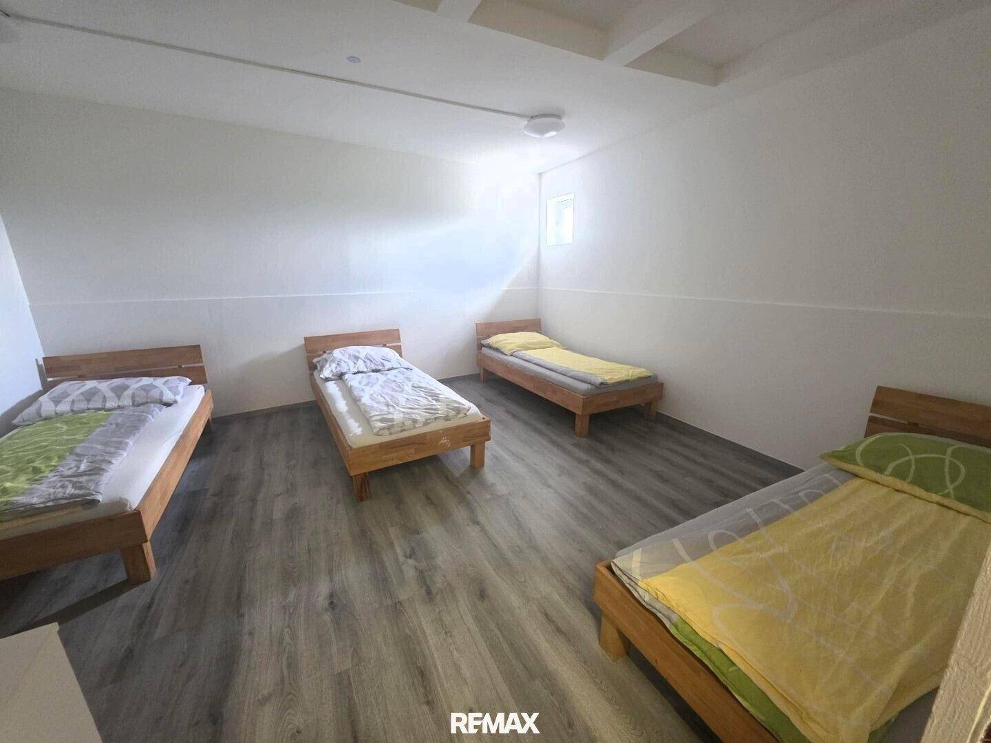 Geräumiges Schlafzimmer mit vier Einzelbetten und Laminatboden, ideal für Gäste.