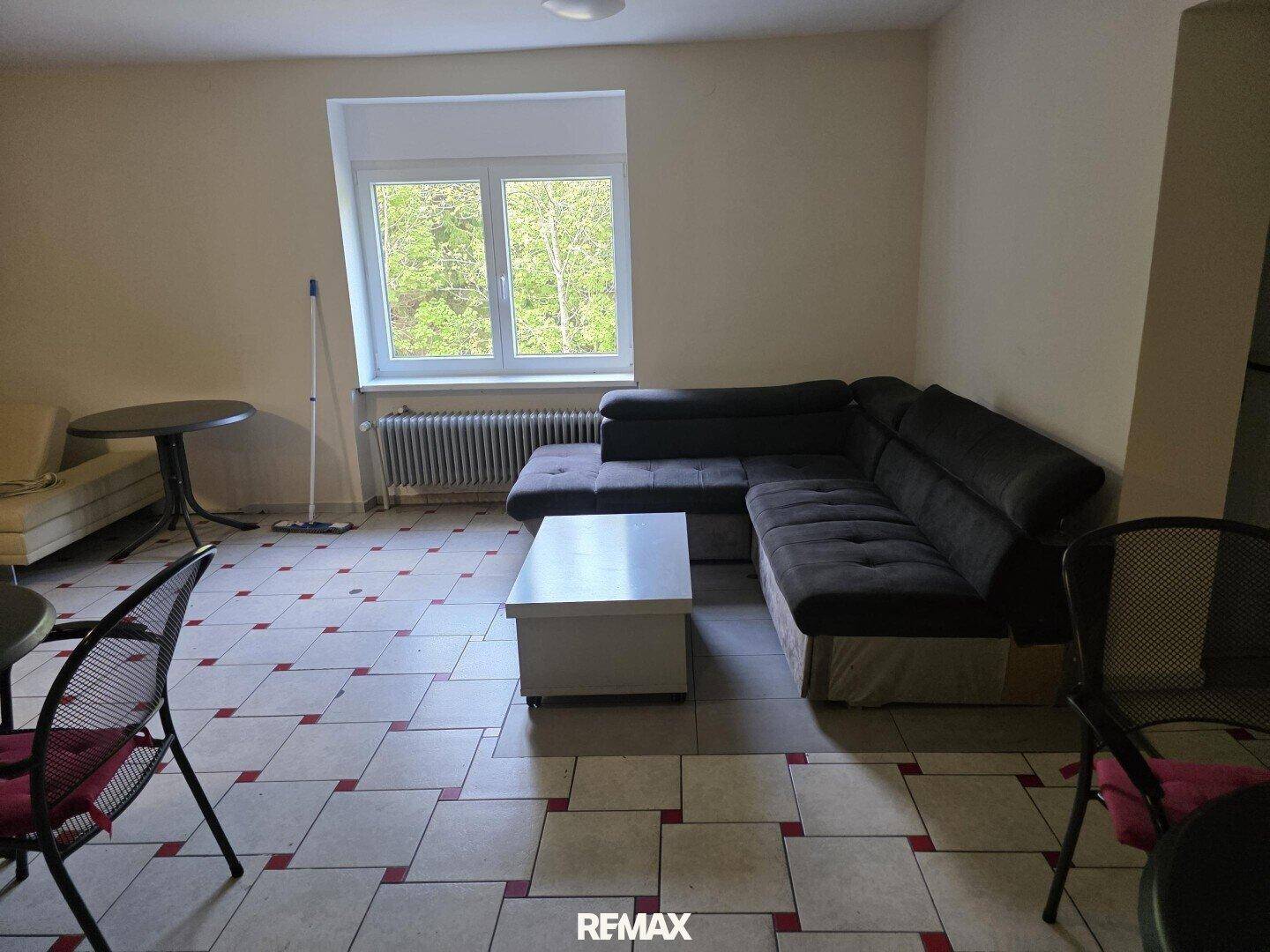Wohnbereich mit großem Sofa, Couchtisch und Tischen, Fliesenboden und Fenster.