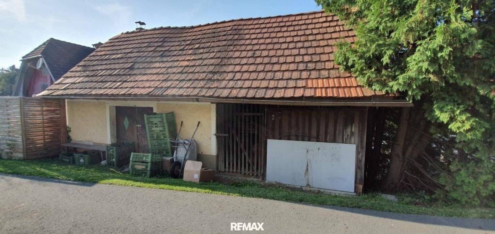 Altes Nebengebäude mit Ziegeldach und Holzwänden, umgeben von Bäumen und Gras.