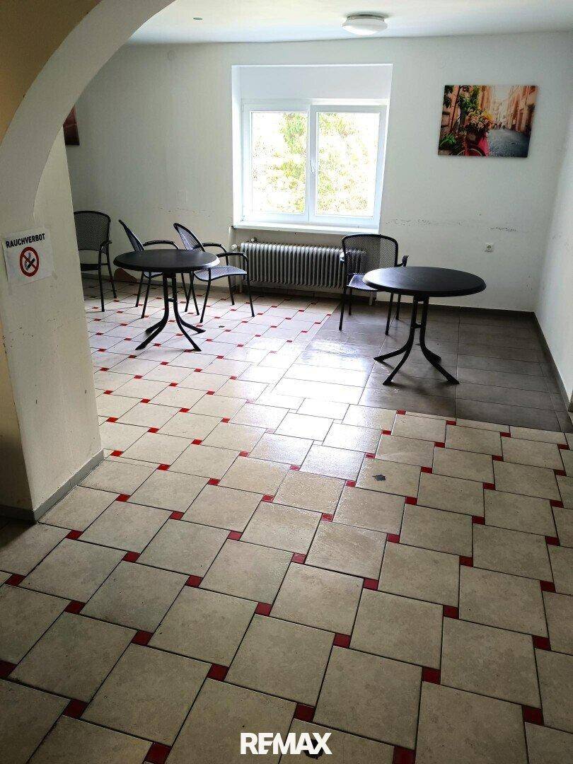 Essbereich mit kleinen Tischen und Stühlen, Fliesenboden und einem Fenster mit Blick ins Grüne.