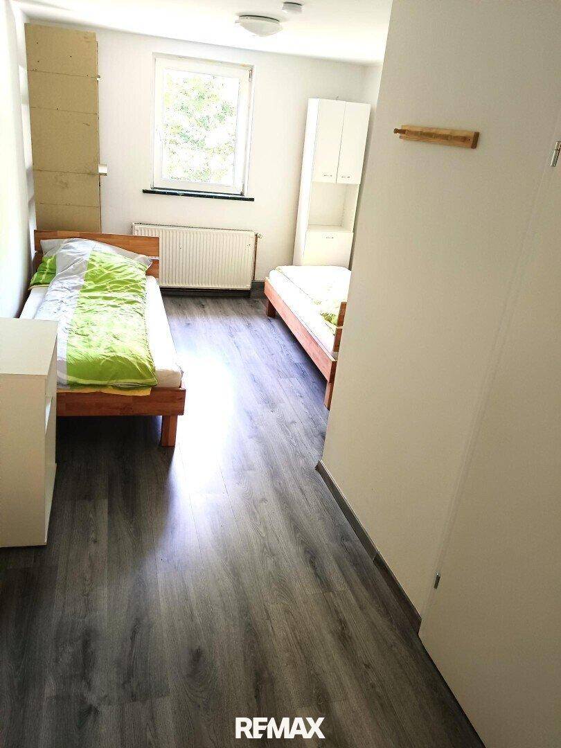 Schlafzimmer mit zwei Einzelbetten, Laminatboden und einem Fenster, das Tageslicht hereinlässt.