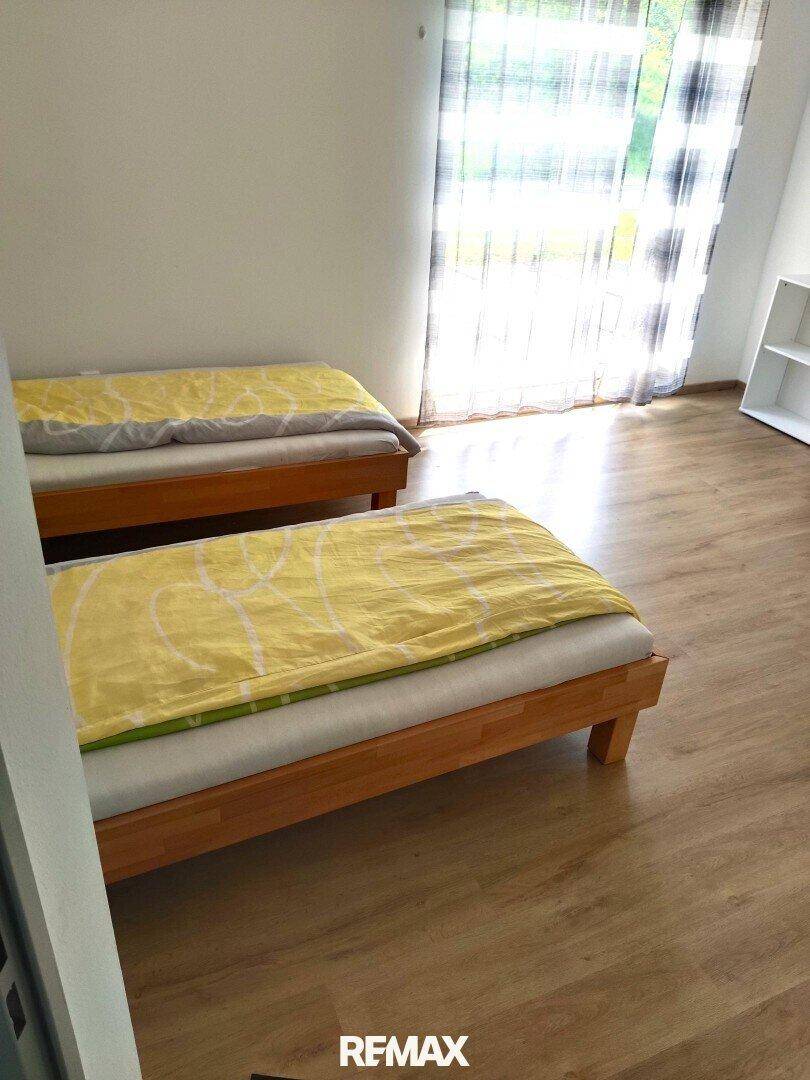 Nahaufnahme von zwei Einzelbetten in einem hellen Schlafzimmer mit Laminatboden.