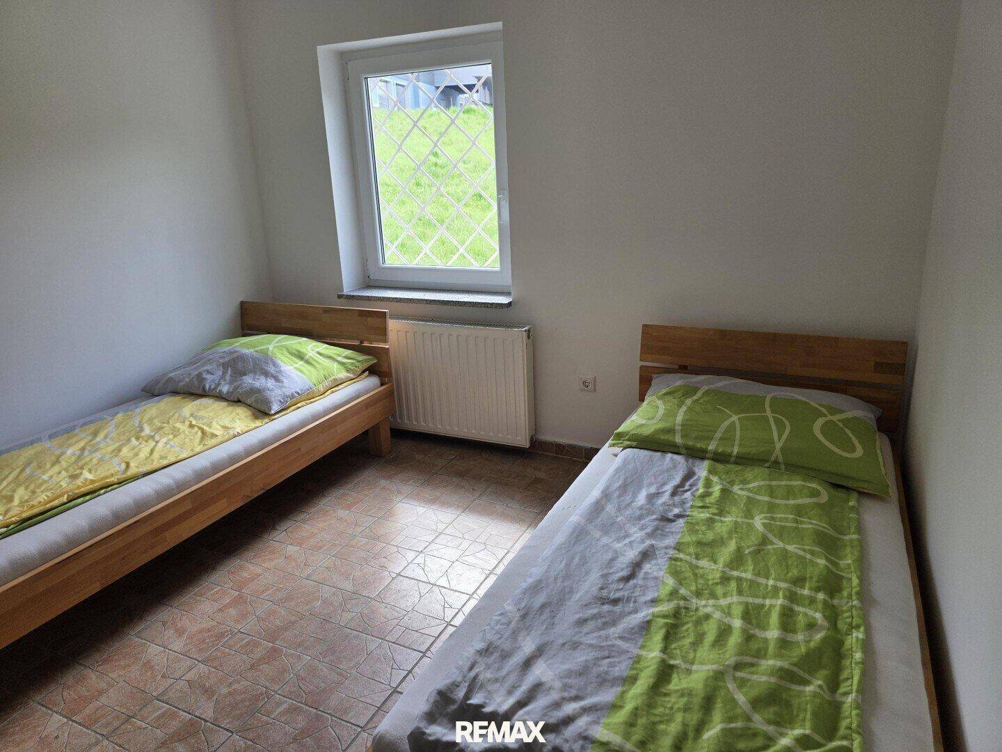 Schlafzimmer mit zwei Einzelbetten und Fliesenboden, das durch ein Fenster belichtet wird.