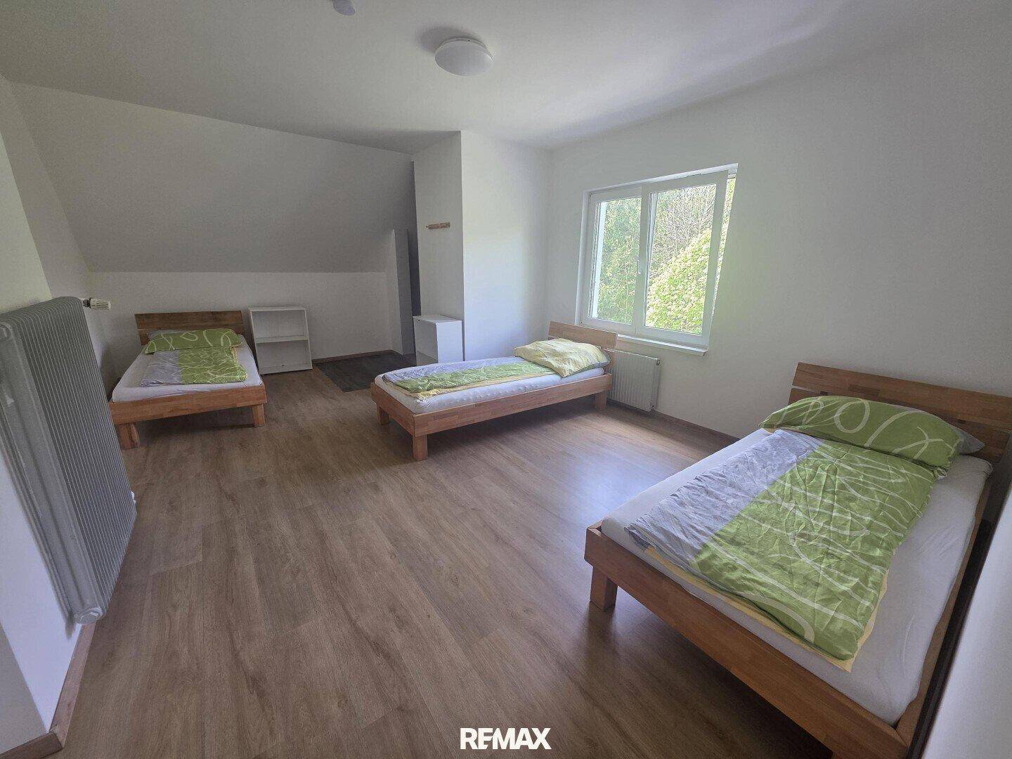 Geräumiges Schlafzimmer mit drei Einzelbetten, Laminatboden und einem Fenster.
