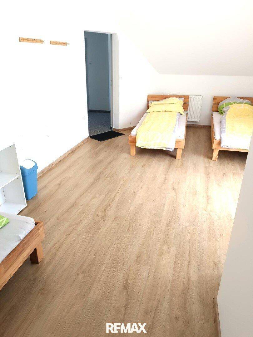 Schlafzimmer mit drei Einzelbetten, Laminatboden und einem Regal, unter Dachschräge.