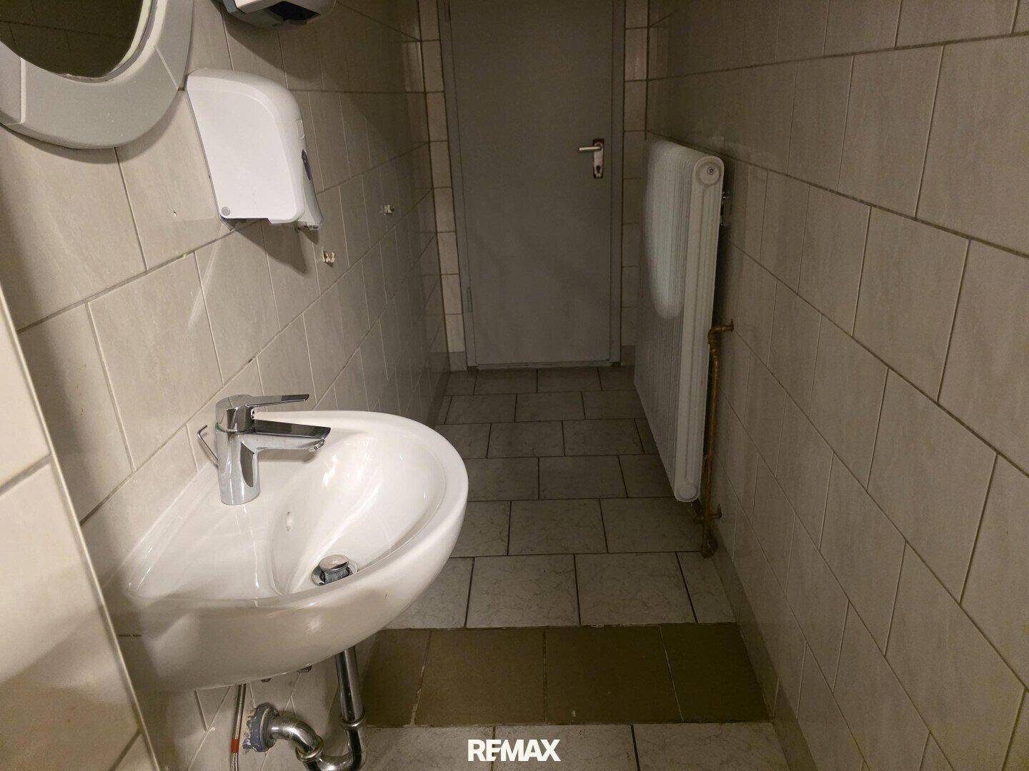 Kleines WC mit Waschbecken, Spiegel und weißen Fliesen.