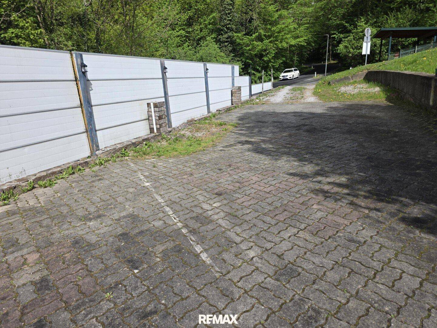 Gepflasterter Außenbereich, der als Parkplatz genutzt werden kann, umgeben von einer Mauer.