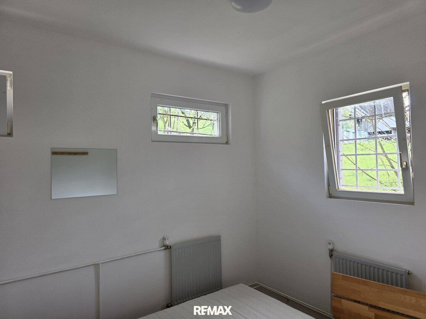 Helles Schlafzimmer mit einem Bett und zwei Fenstern, die viel Tageslicht hereinlassen.