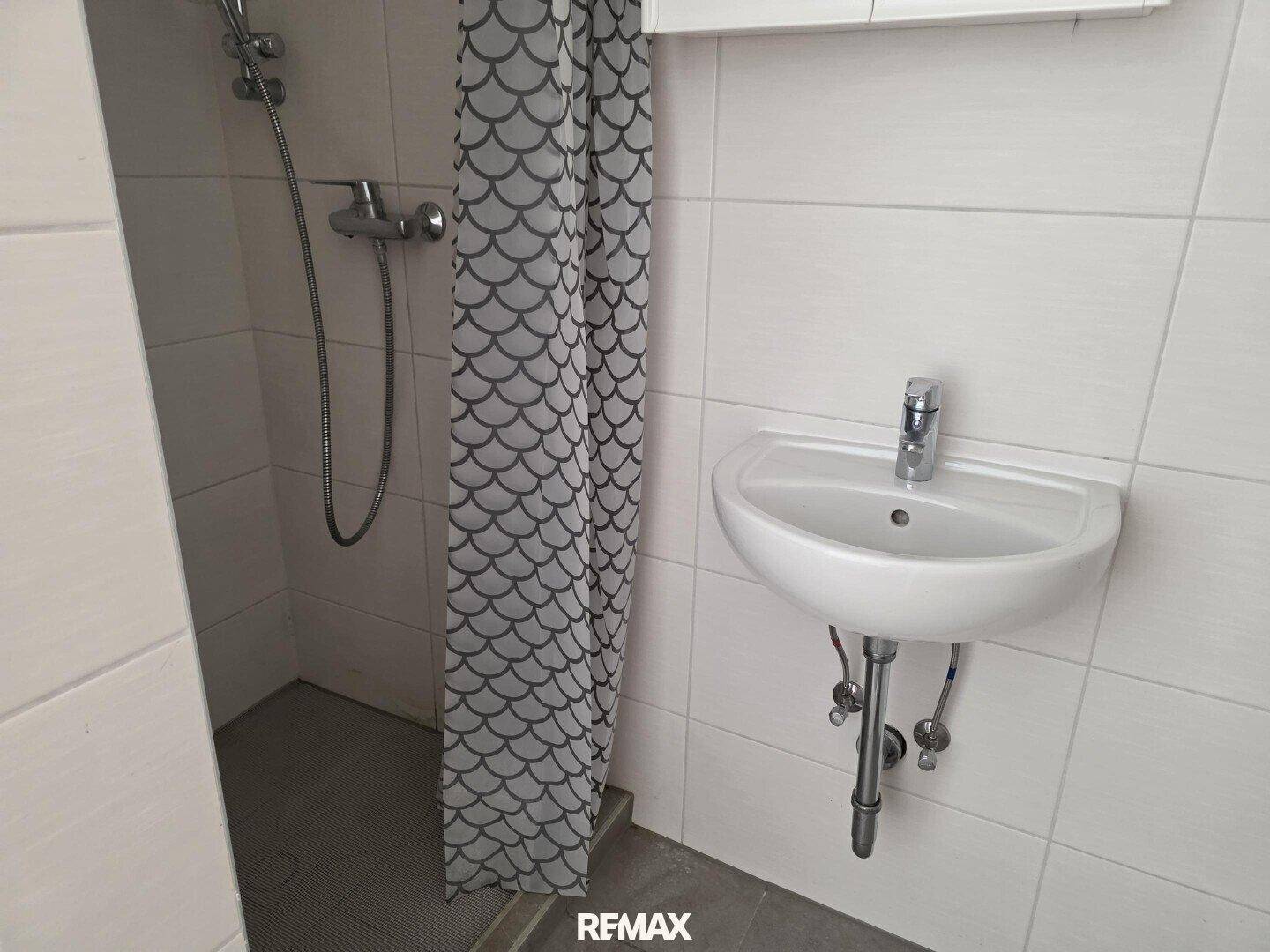 Badezimmer mit Waschbecken und Duschbereich, ausgestattet mit weißen Fliesen.