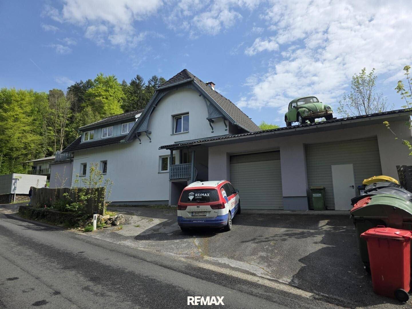 Gut erhaltenes Haus mit Garage, geparktem Auto und einem Oldtimer auf dem Garagendach.