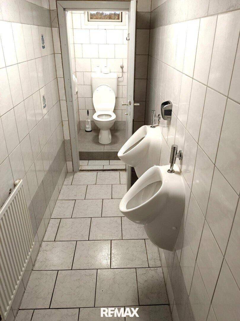 Gefliestes WC mit zwei Urinalen und einer separaten Toilettenkabine.